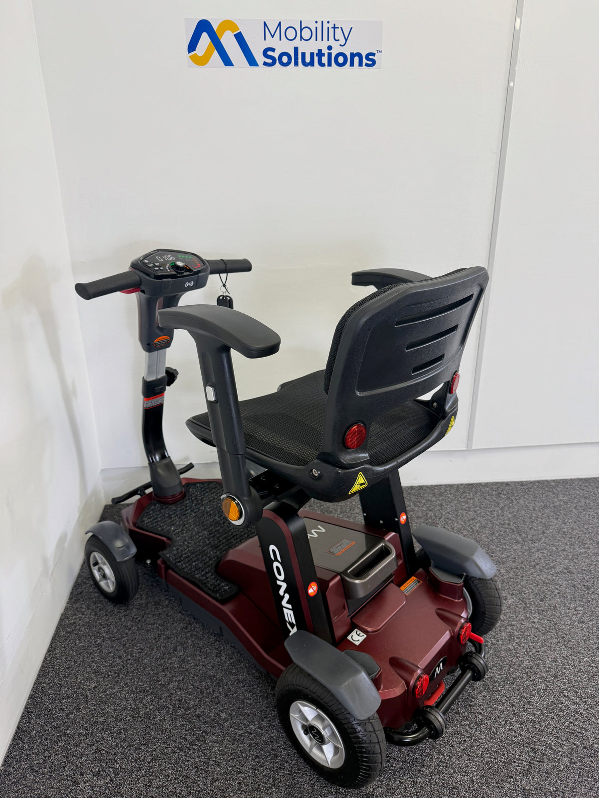 Mobility scooter with 'Mobility Solutions' logo on a white wall background