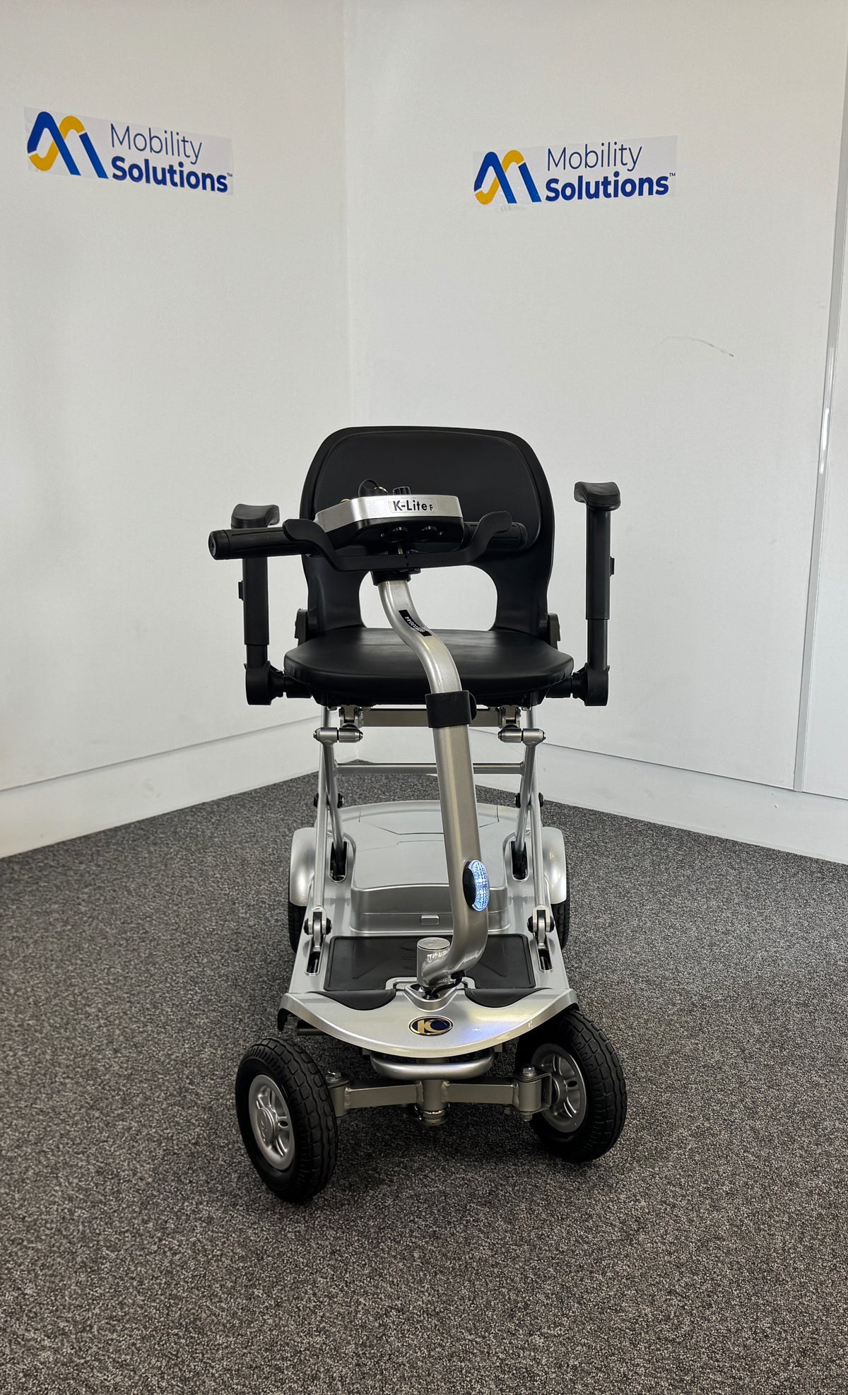 Mobility scooter with a seat in a room with 'Mobility Solutions' branding.